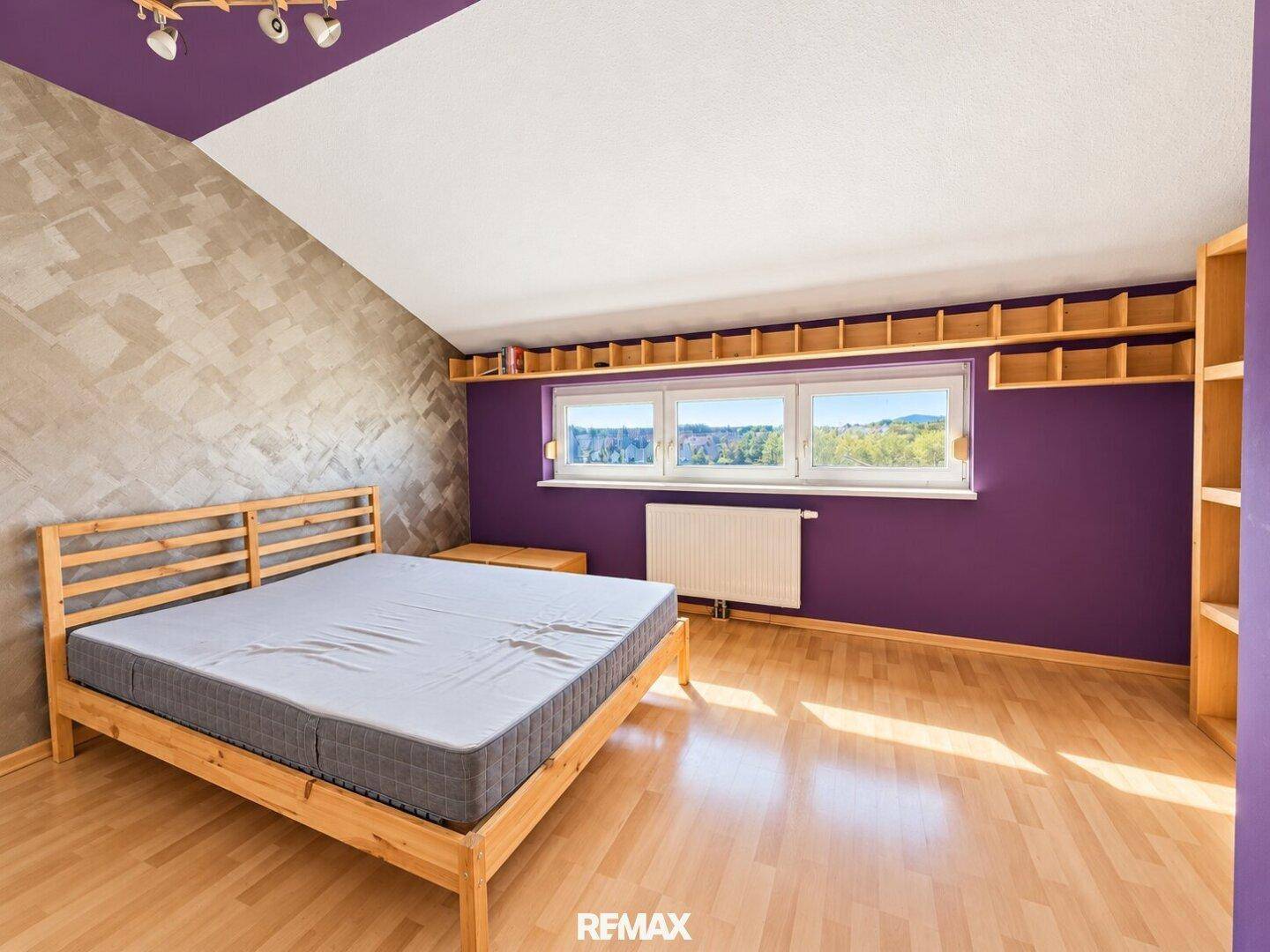 Helles Schlafzimmer mit Holzbett, Parkettboden und weitem Ausblick aus dem Fenster.