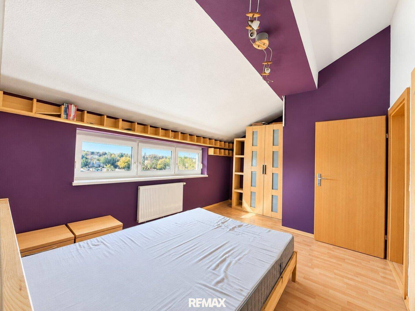 Schlafzimmer mit Fenster, Holzboden und praktischen eingebauten Regalen.