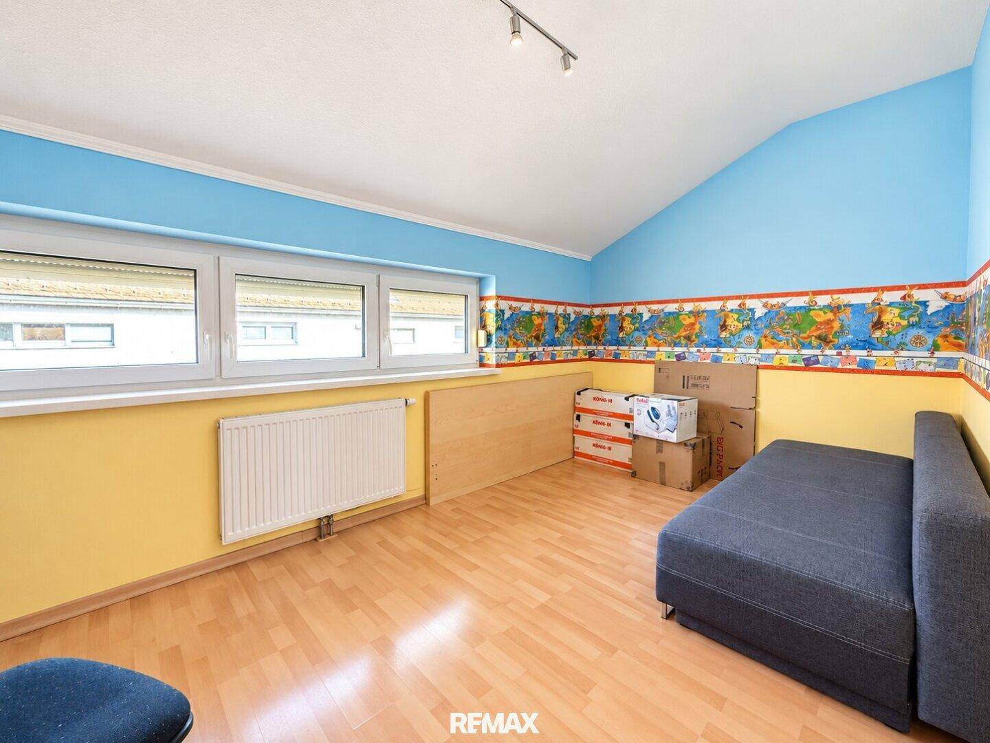 Helles Zimmer mit farbenfrohen Wänden, Parkettboden und einem Schlafsofa.