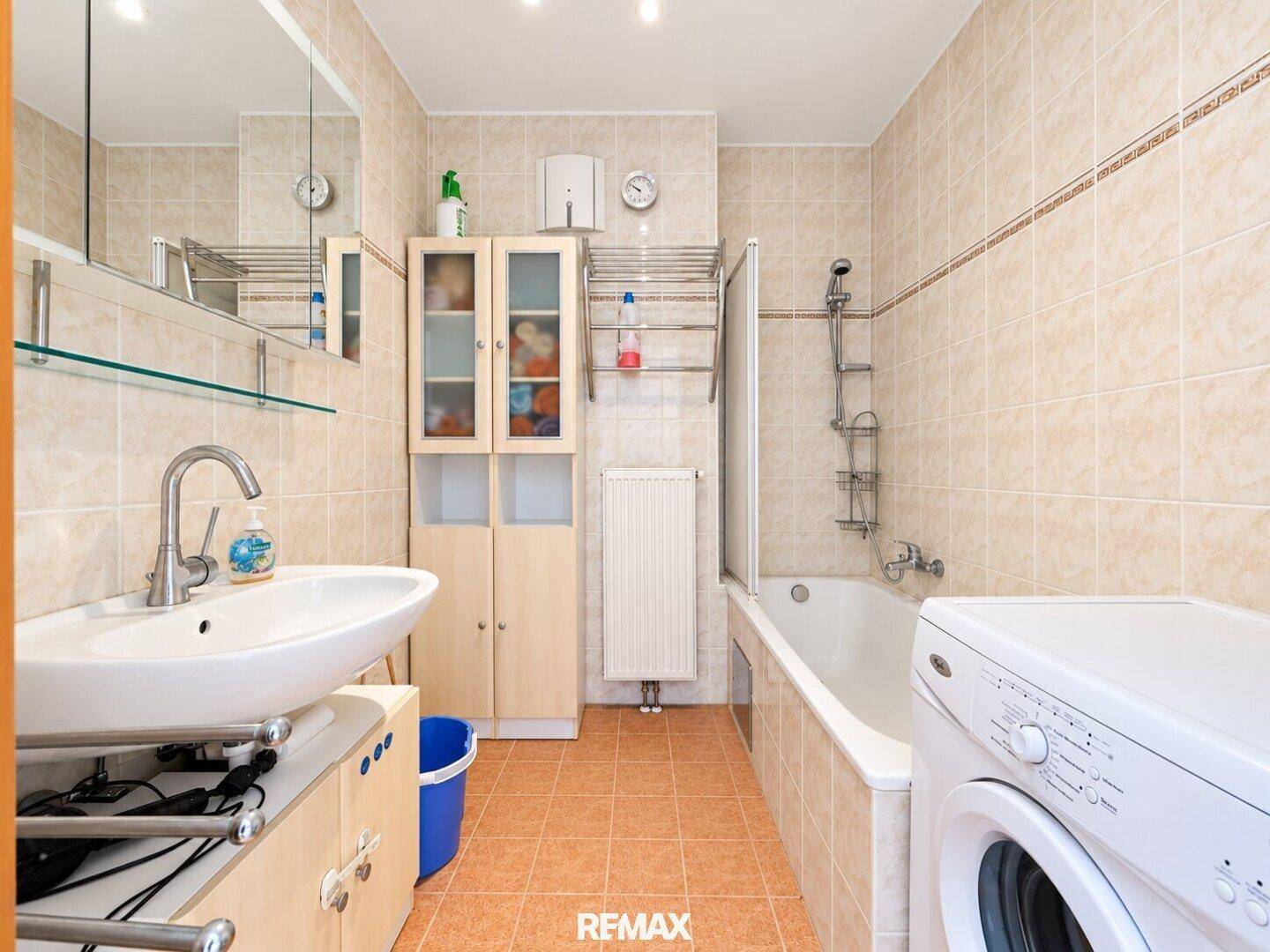 Badezimmer mit Badewanne, Waschbecken, Waschmaschine und beigefarbenen Fliesen.