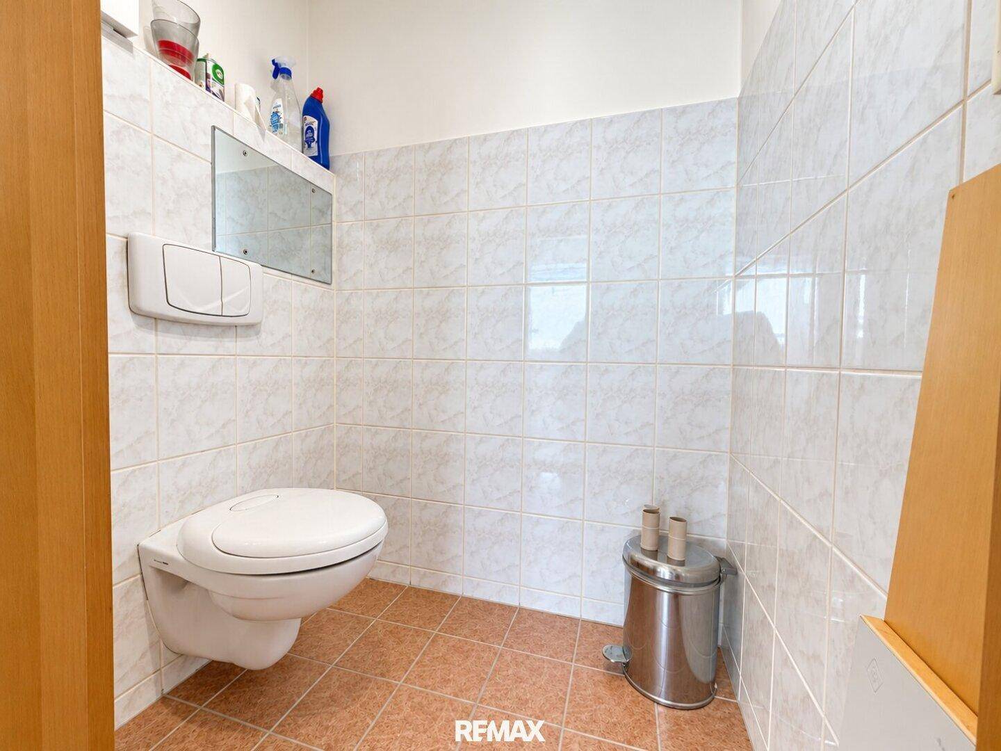 Separates WC mit wandhängender Toilette und hellen Fliesen an Wänden und Boden.