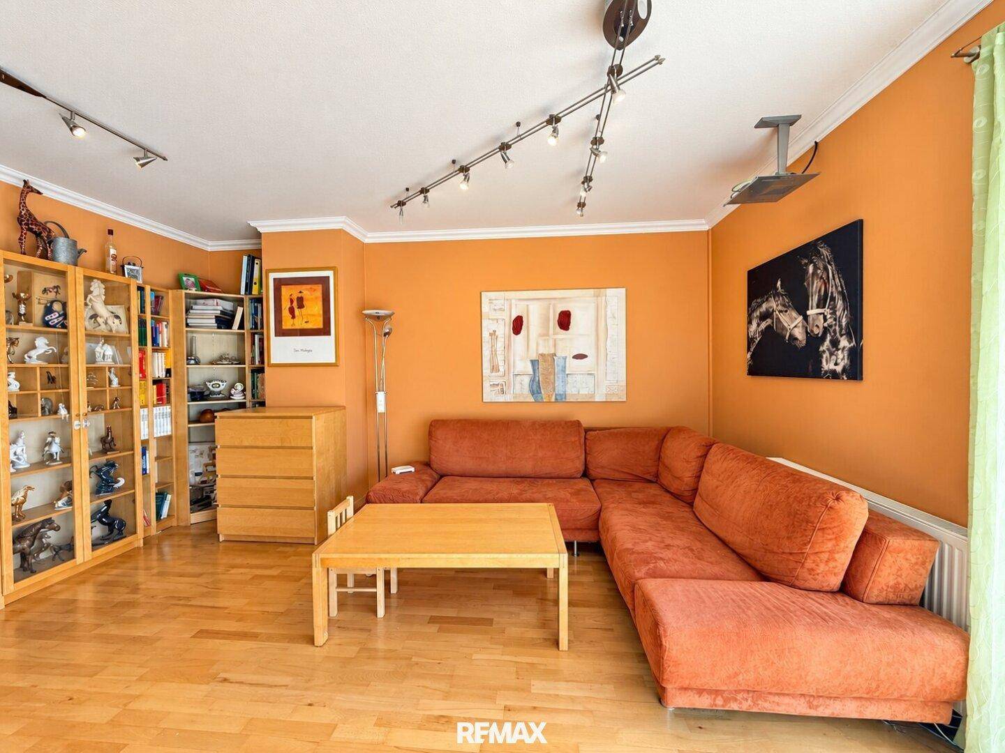 Gemütlicher Wohnbereich mit großem Ecksofa, Parkettboden und orangefarbenen Wänden.