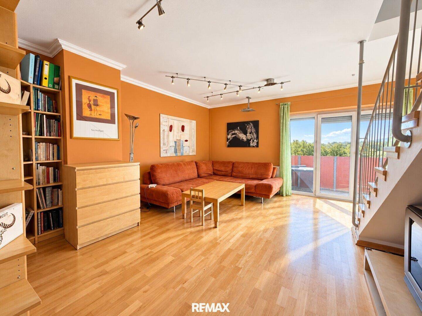 Helles Wohnzimmer mit Parkettboden, Zugang zum Balkon und gemütlicher Sitzecke.