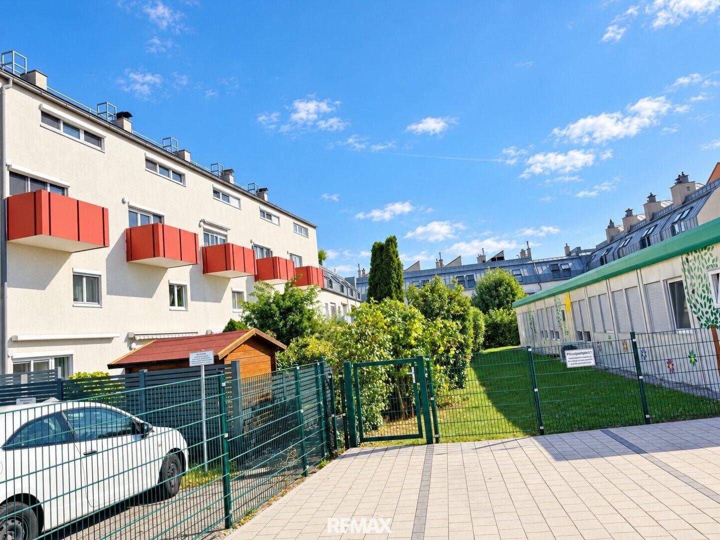 Außenansicht eines Wohnkomplexes mit Grünflächen und einem geparkten Auto.