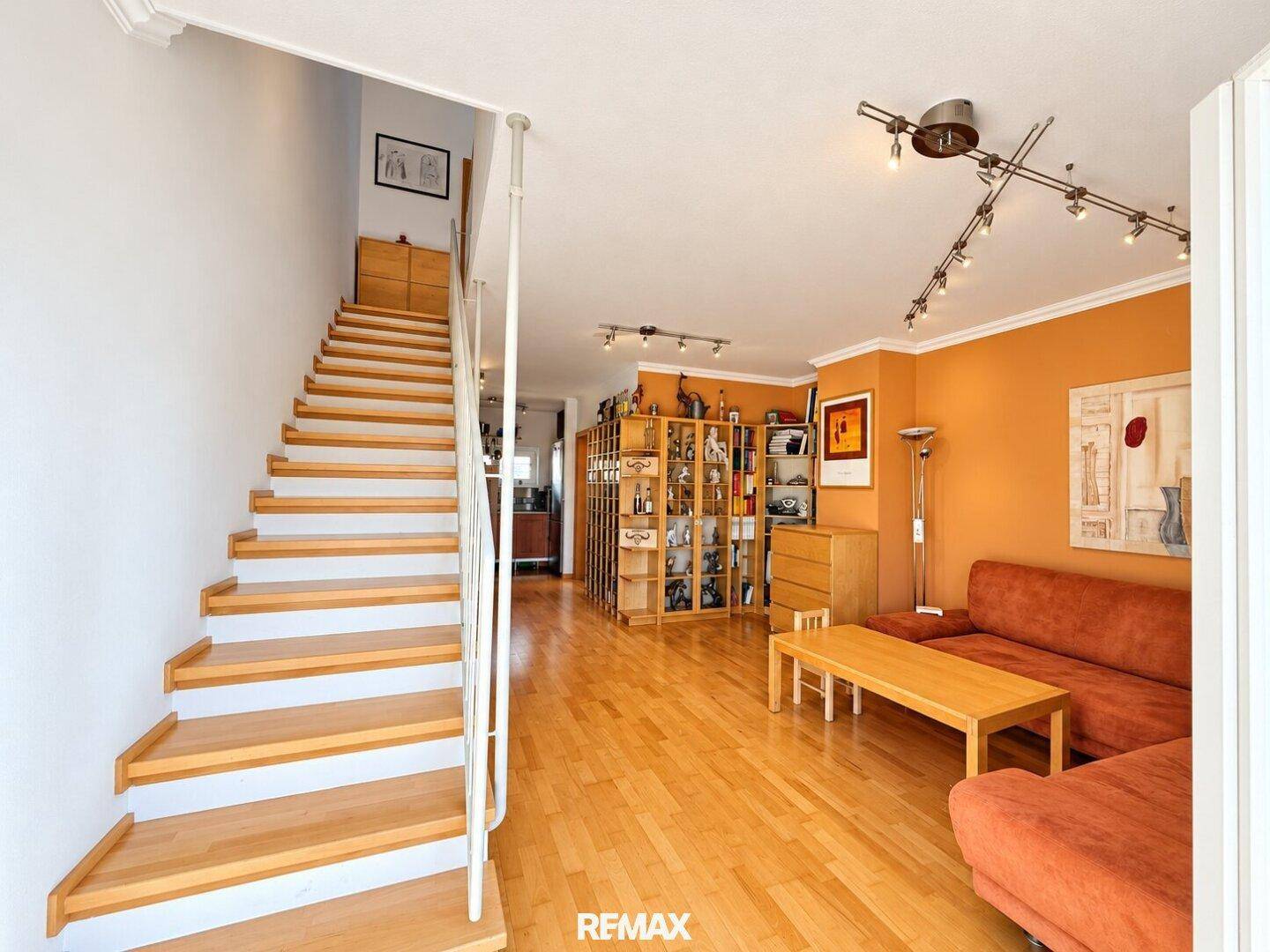 Gemütliches Wohnzimmer mit Holztreppe, Parkettboden und orangefarbenen Wänden.