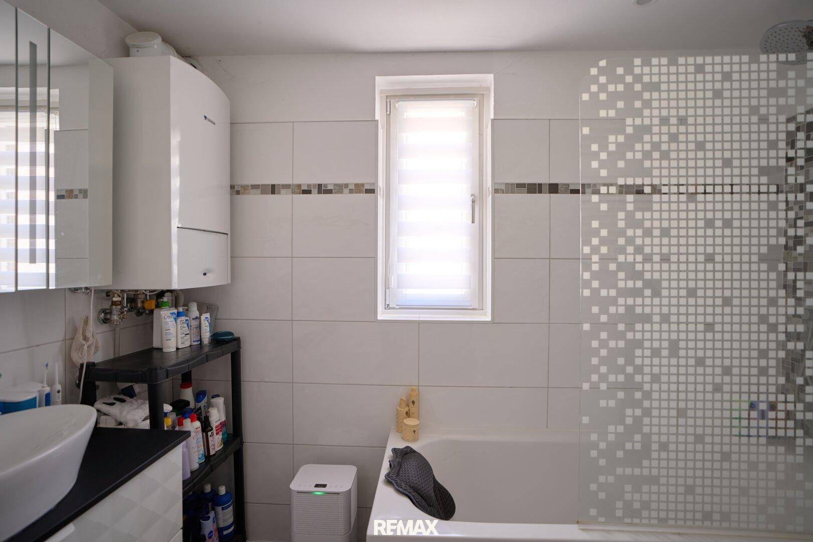 Modernes Badezimmer mit Badewanne, Fenster und weißen Fliesen.