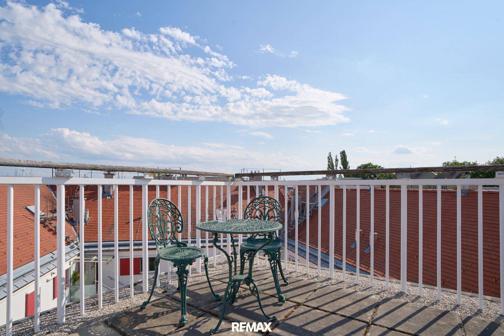 Geräumige Dachterrasse mit Metallgeländer und Sitzgelegenheiten unter blauem Himmel.