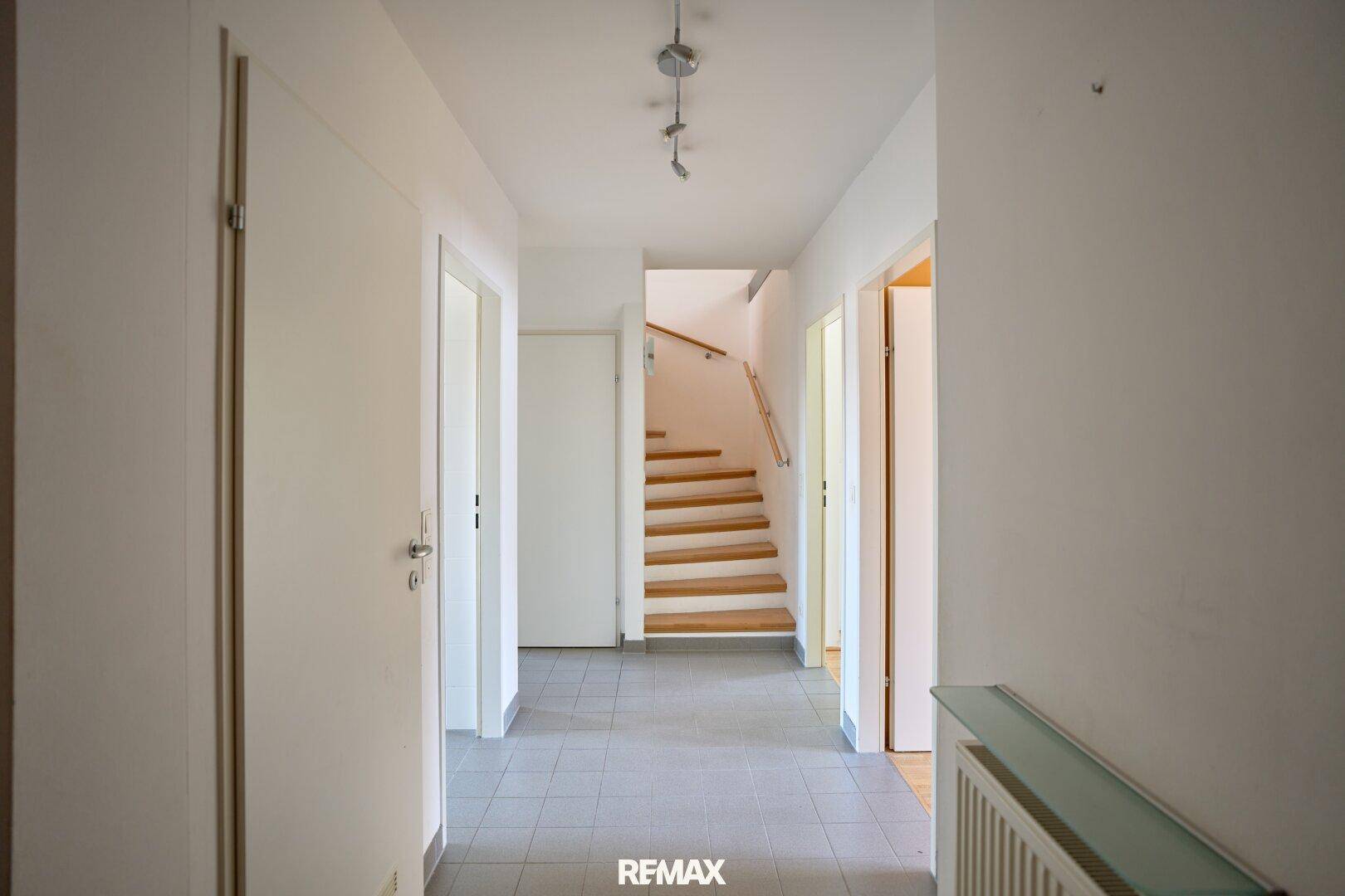 Heller Flur mit Fliesenboden und Zugang zu weiteren Räumen sowie einer Holztreppe.
