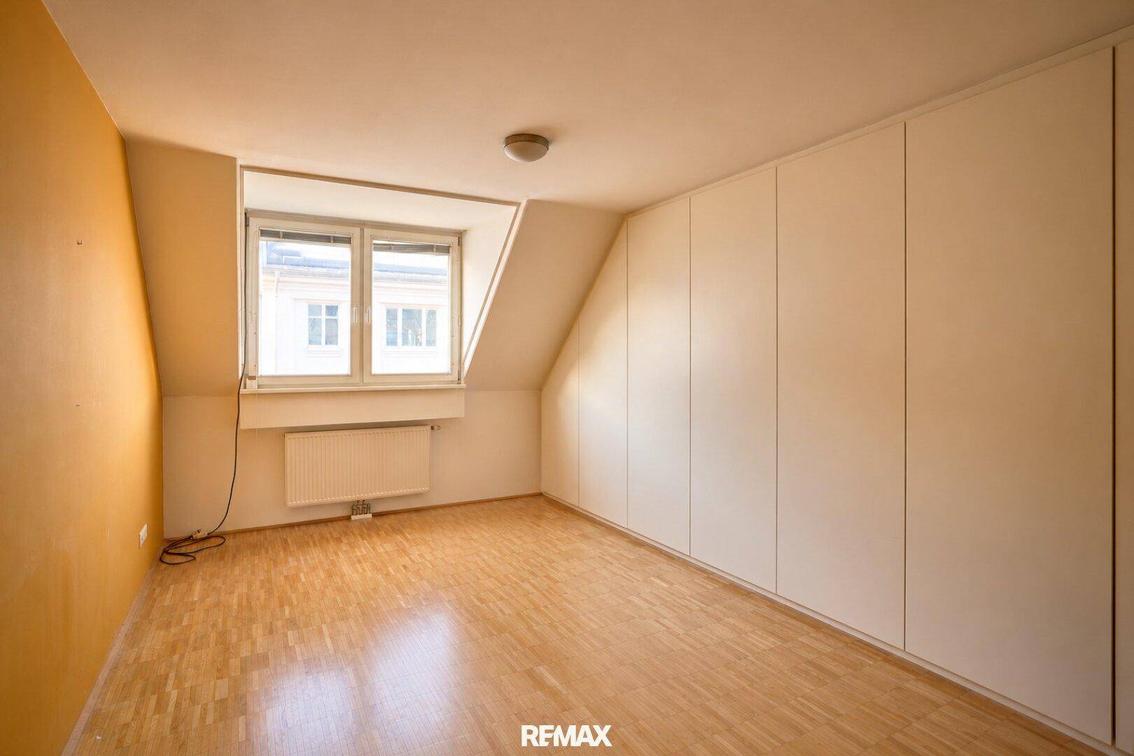 Schlafzimmer mit Dachschräge, Parkettboden und Einbauschränken entlang einer Wand.