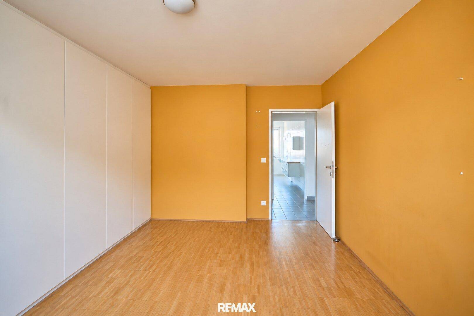 Geräumiges Schlafzimmer mit Parkettboden, gelber Akzentwand und Einbauschränken.