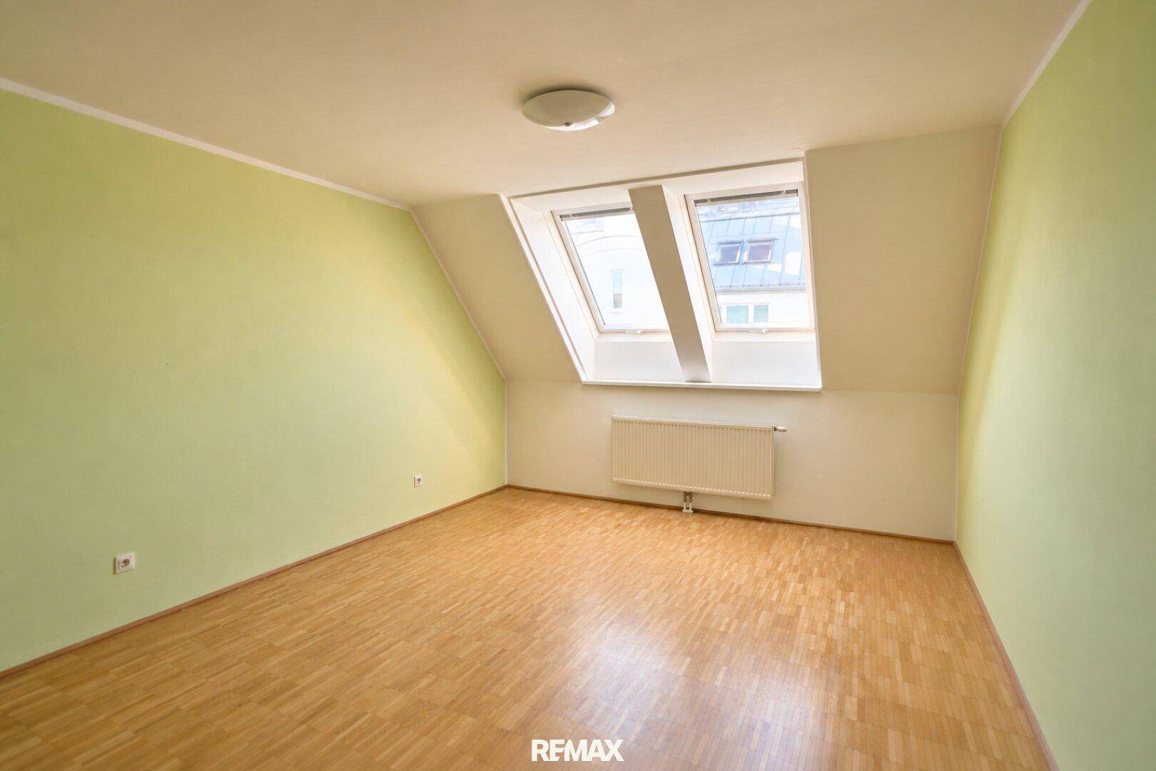 Helles Schlafzimmer mit Parkettboden, grünen Wänden und Dachfenstern für viel Licht.