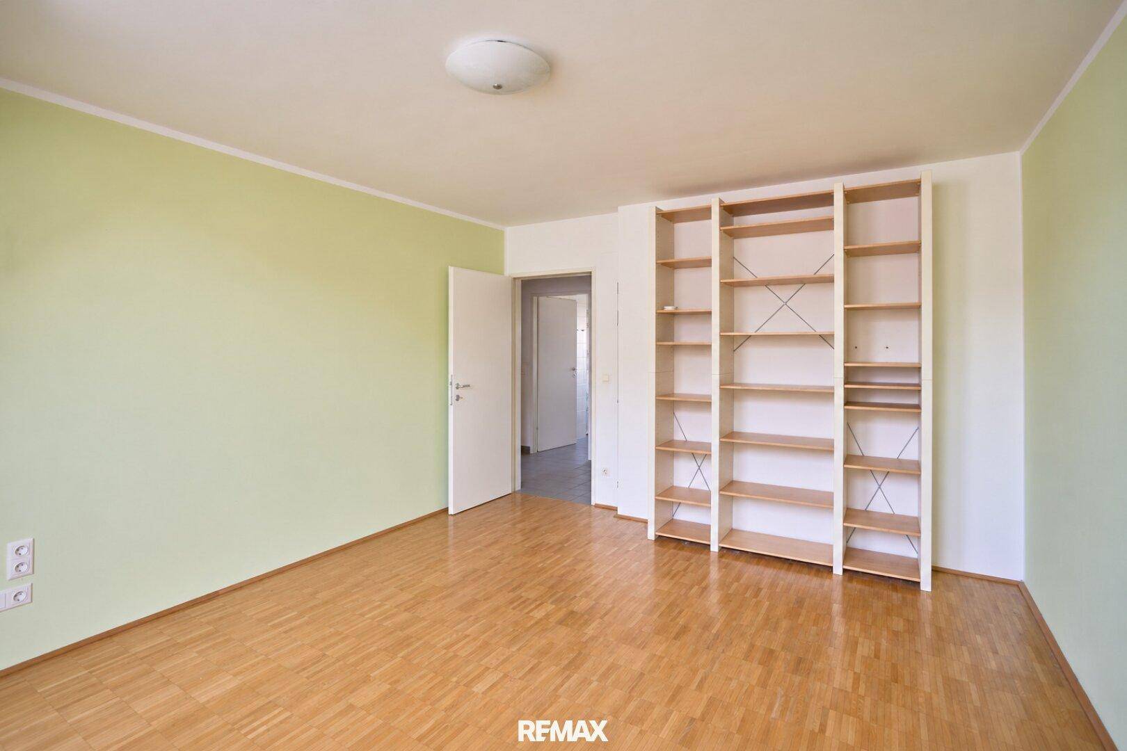 Schlafzimmer mit Parkettboden, grünen Wänden und einem großen Bücherregal.