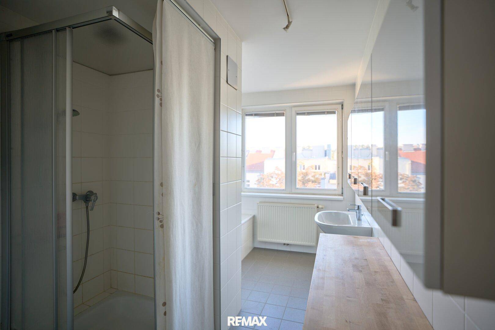 Modernes Badezimmer mit Dusche, Fenster und hellem Fliesenboden.
