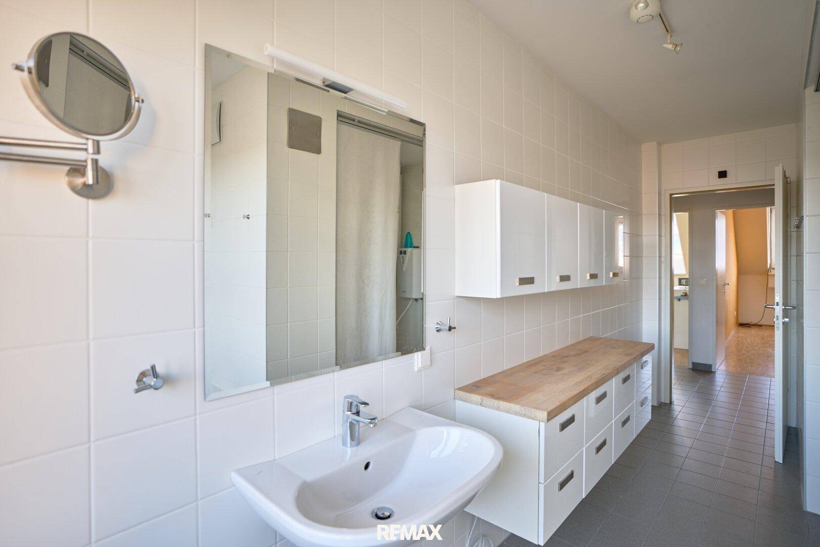 Helles Badezimmer mit Waschbecken, Spiegel und Holzablagefläche.