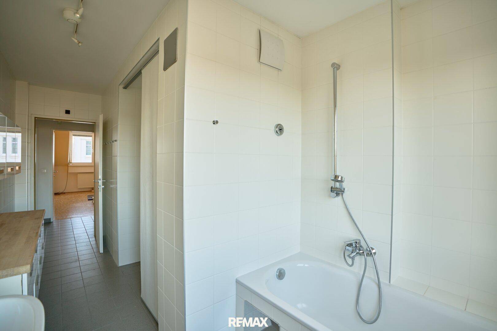 Badezimmer mit Badewanne, weißen Fliesen und Blick in den Flur.