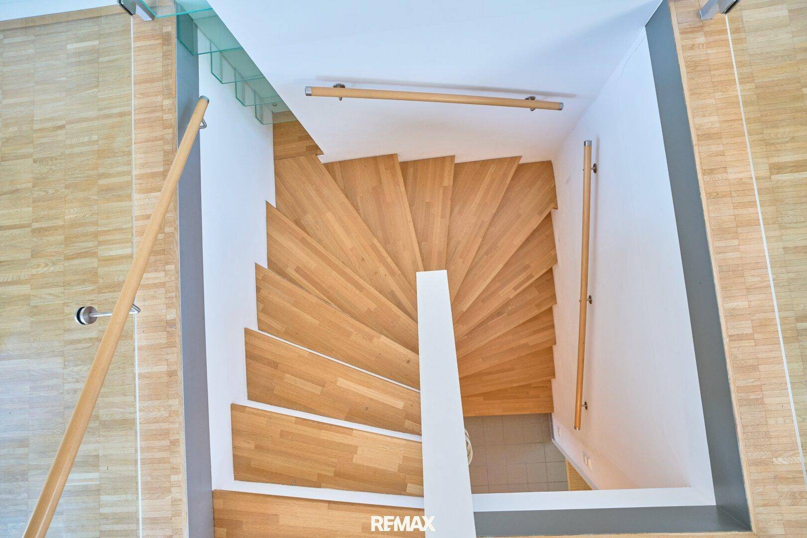Holztreppe mit Glasgeländer, die die verschiedenen Ebenen der Wohnung verbindet.