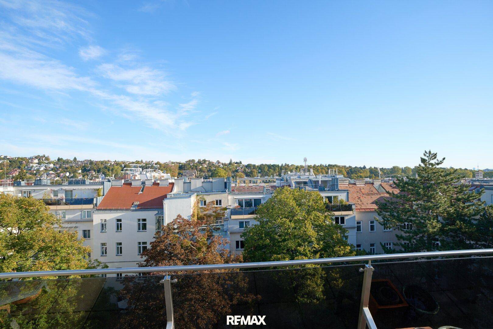 Weitläufiger Blick vom Balkon über die grüne Umgebung und die Dächer der Stadt.