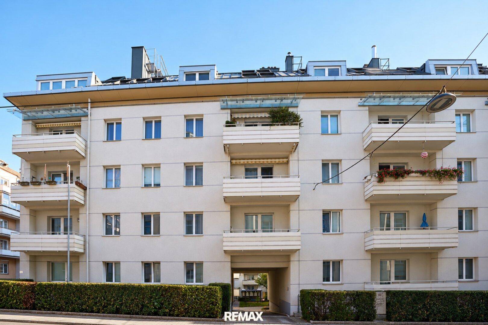 Mehrfamilienhaus mit Balkonen, grüner Hecke und moderner Architektur.