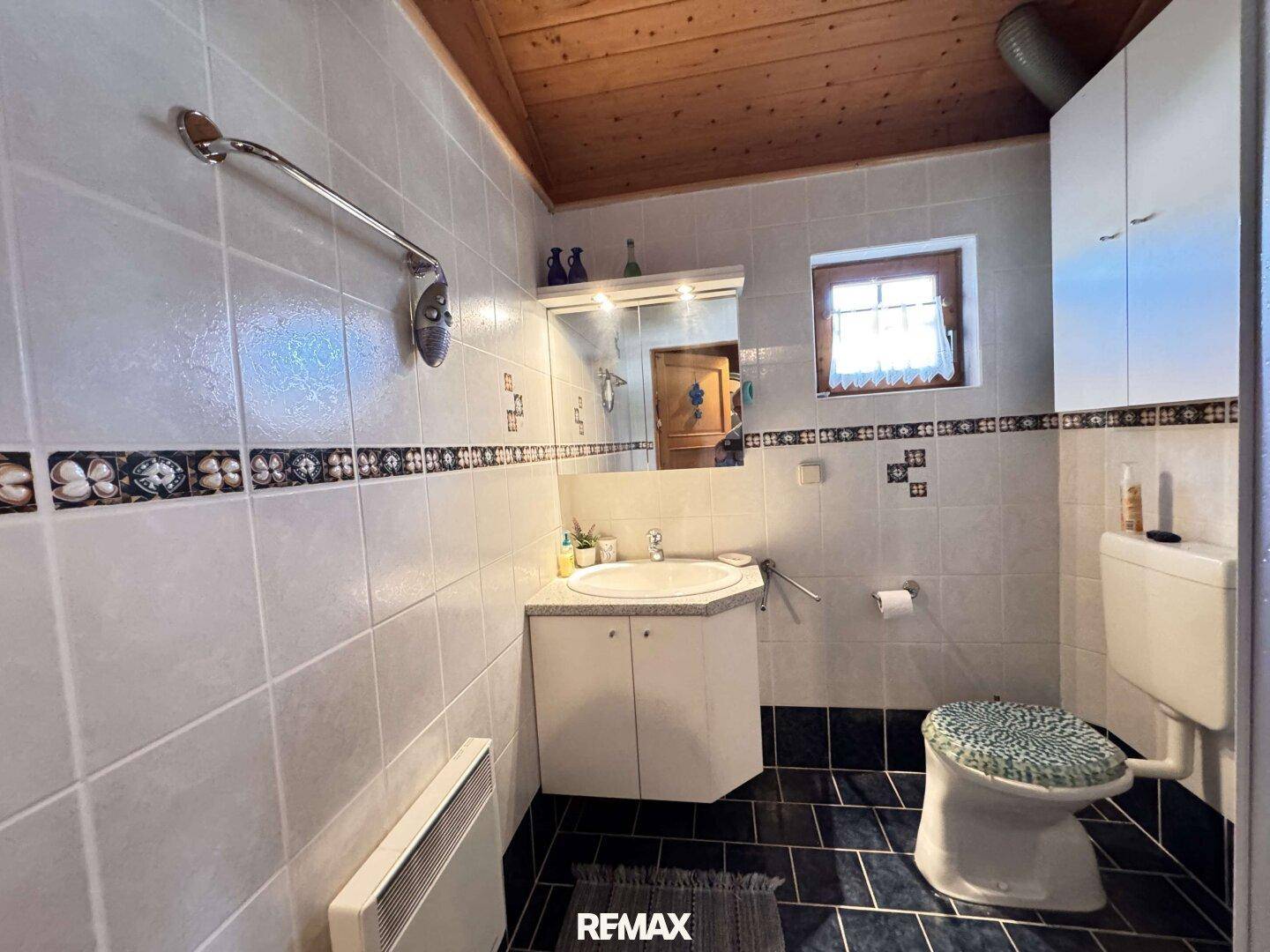 Badezimmer mit weißen Wandfliesen, dunklem Fliesenboden und einem Fenster für Tageslicht.