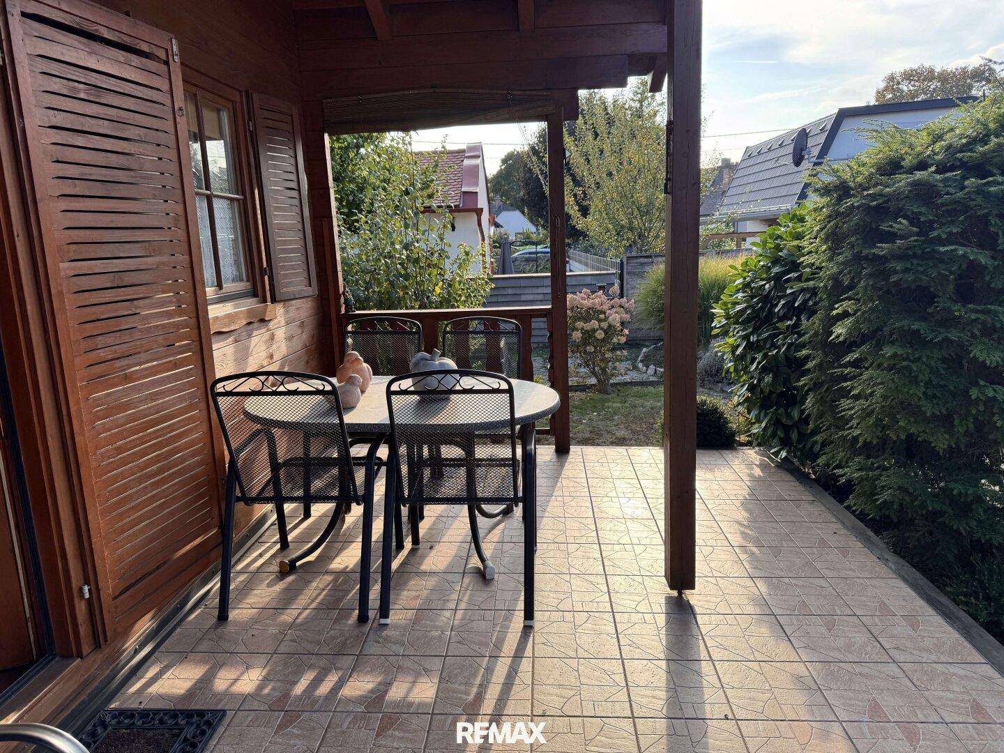Überdachte Terrasse mit Fliesenboden und Gartenmöbeln, ideal für entspannte Stunden im Freien.