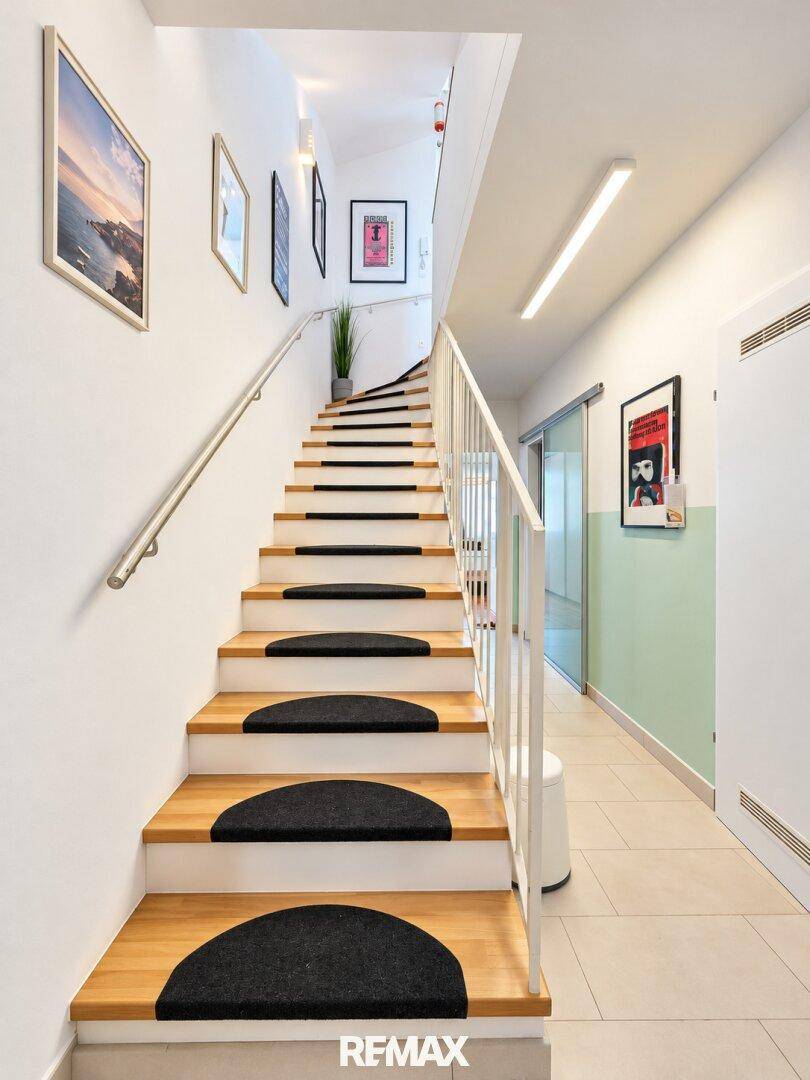 Holztreppe mit Teppichstufen und modernem Geländer in einem hellen Flur.