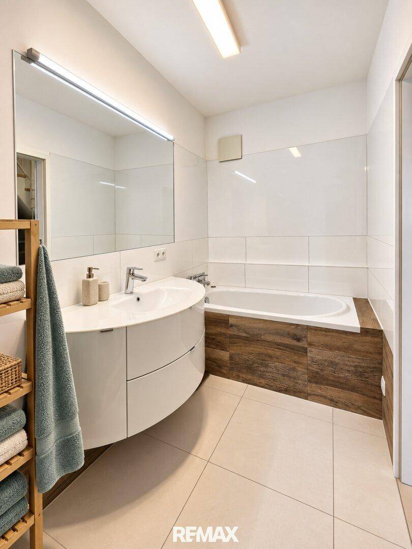 Modernes Badezimmer mit Badewanne, Einzelwaschbecken und großem Spiegel.