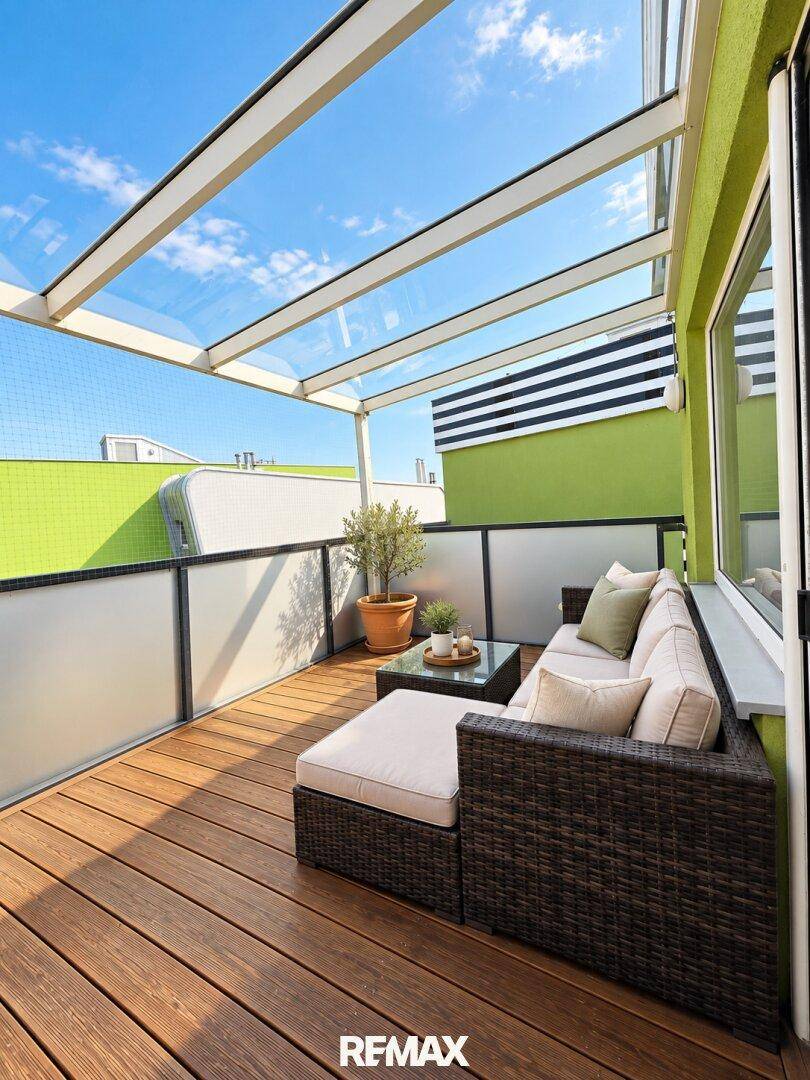 Überdachter Balkon mit Holzboden, Lounge-Möbeln und Glasdach.
