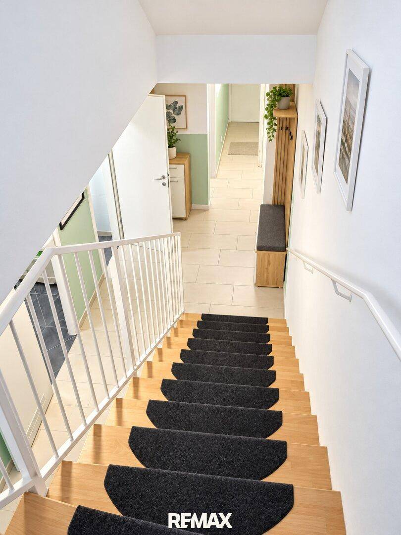 Blick vom Treppenhaus in den hellen Flur mit Garderobe und Fliesenboden.