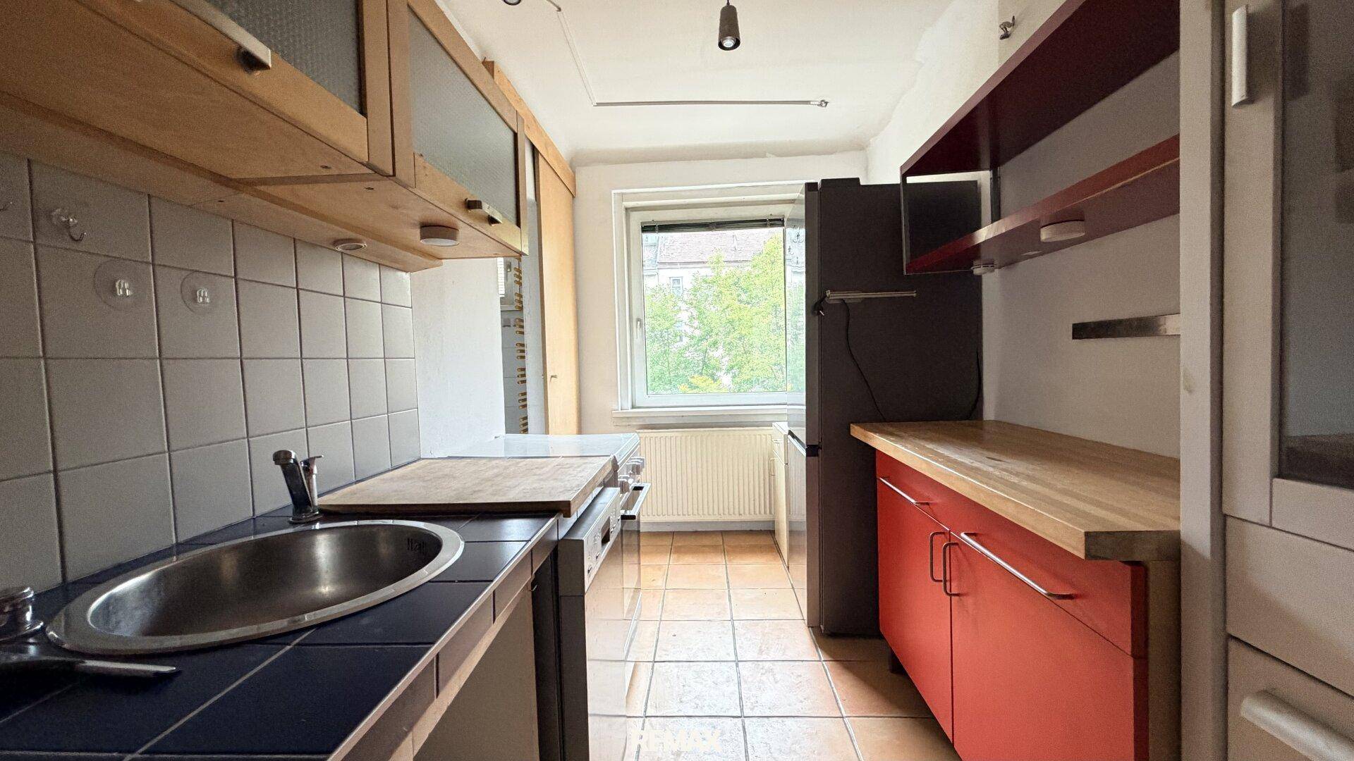 Funktionale Küche mit roten Unterschränken, Holzarbeitsplatten und Fenster mit Grünblick.