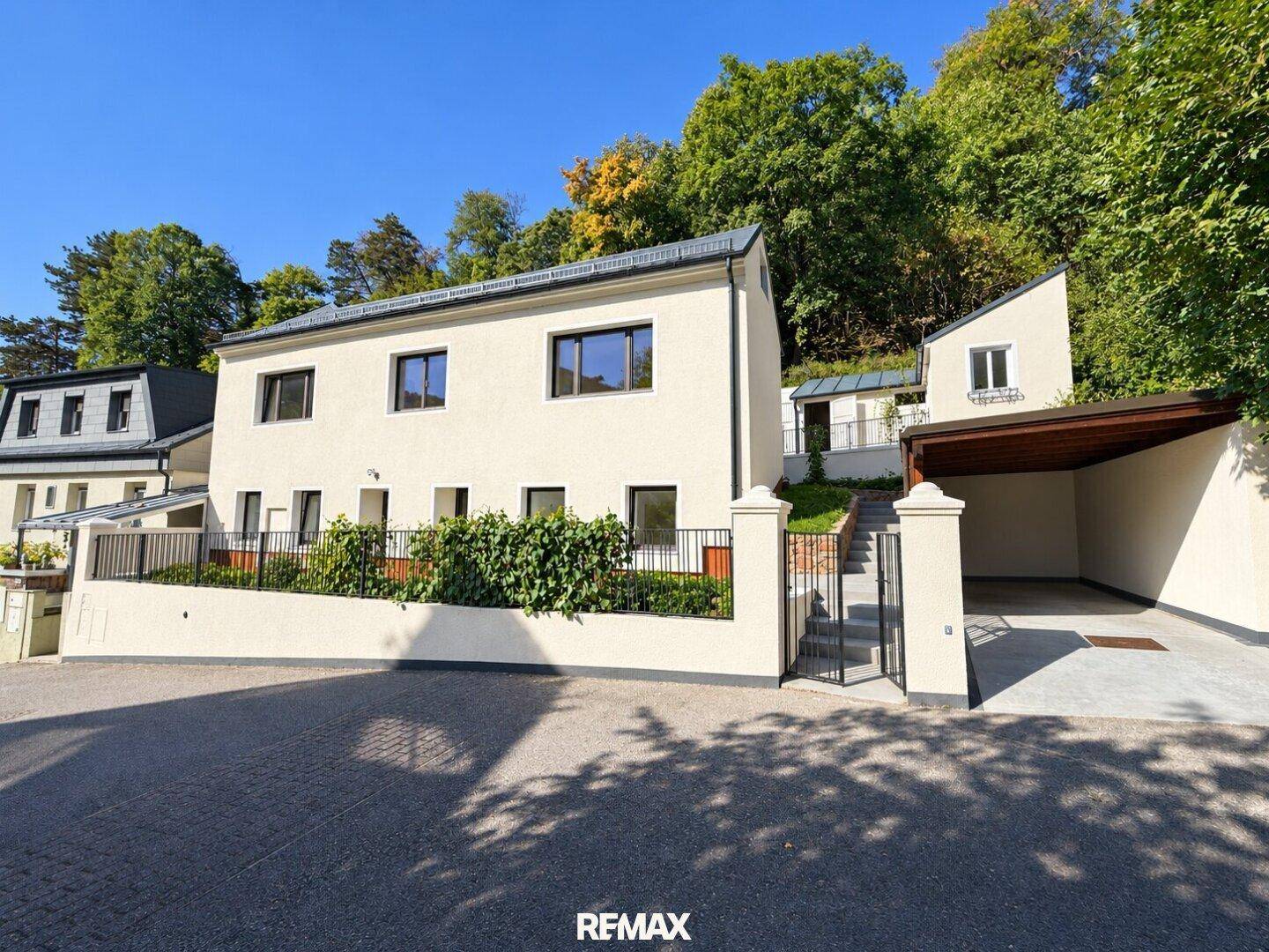 Moderne Wohngebäude mit weißer Fassade, Carport und grüner Hanglage.