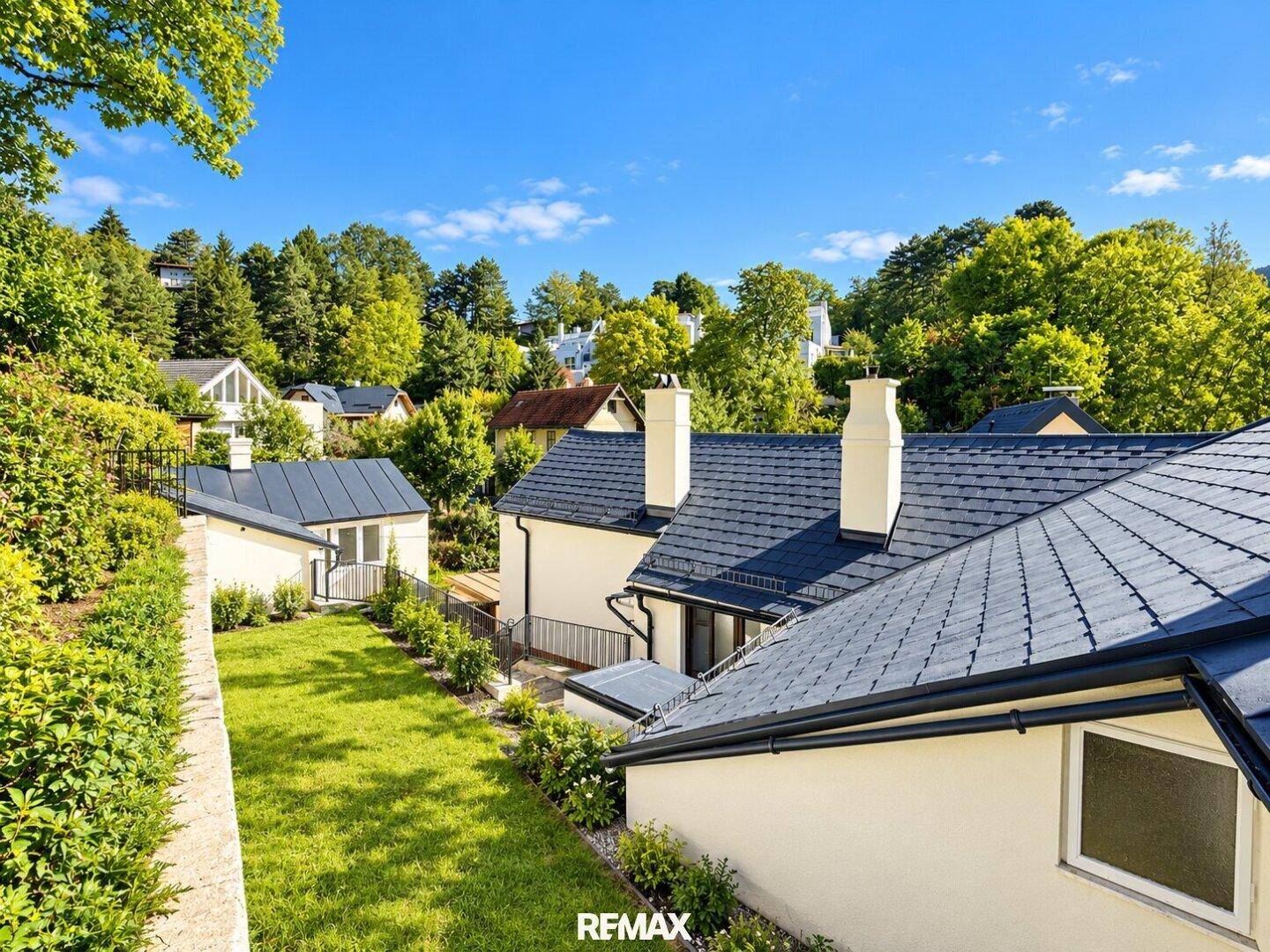 Gepflegter Gartenbereich hinter dem Haus mit dunklem Dach und grüner Bepflanzung.