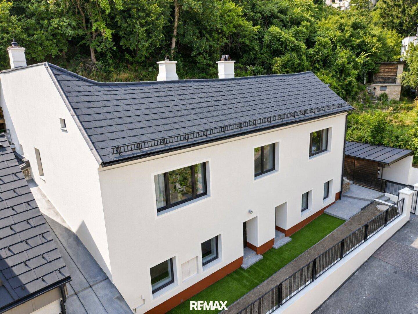 Draufsicht auf das Wohnhaus mit weißer Fassade, dunklem Dach und gepflegtem Vorgarten.