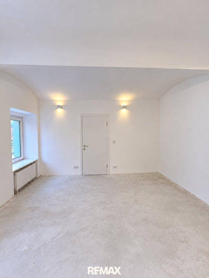Leerer Raum mit weißen Wänden, Betonboden und Fenster mit Heizkörper.