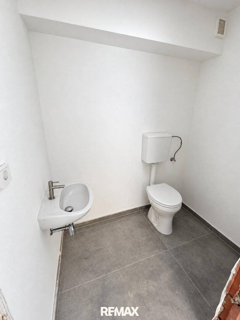 Kleines Gäste-WC mit Toilette, Waschbecken und grauen Bodenfliesen.