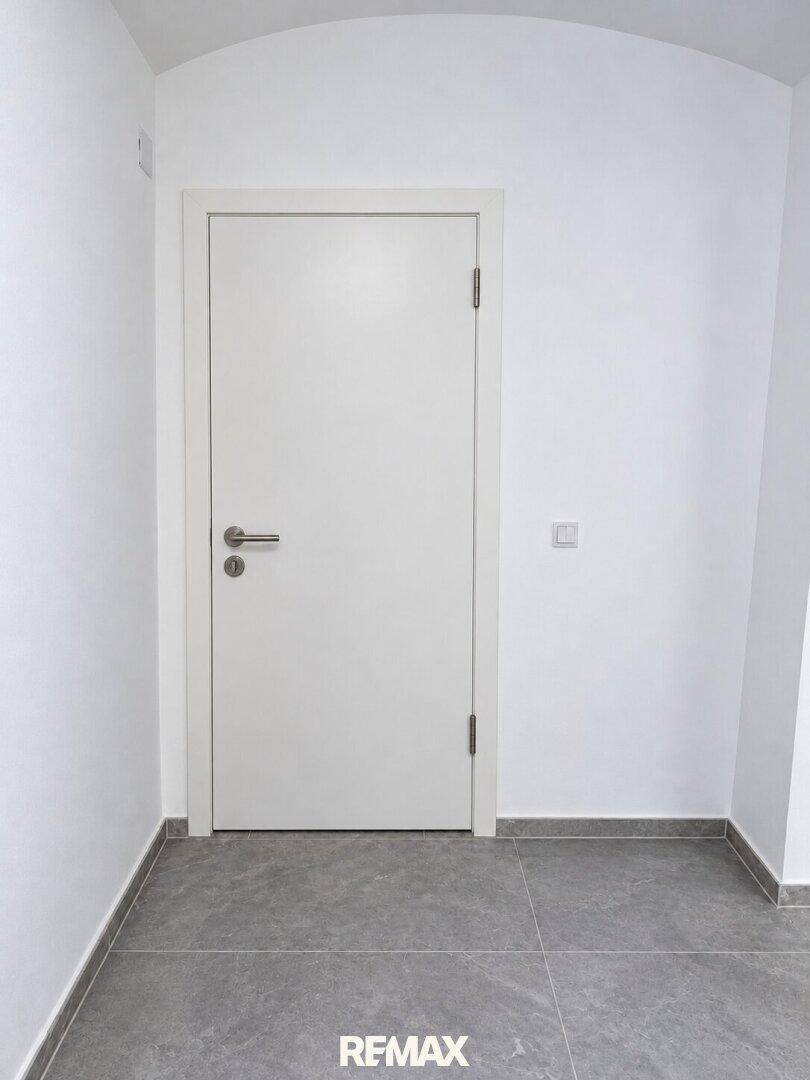 Heller Flur mit weißer Tür, grauen Fliesen und minimalistischem Design.