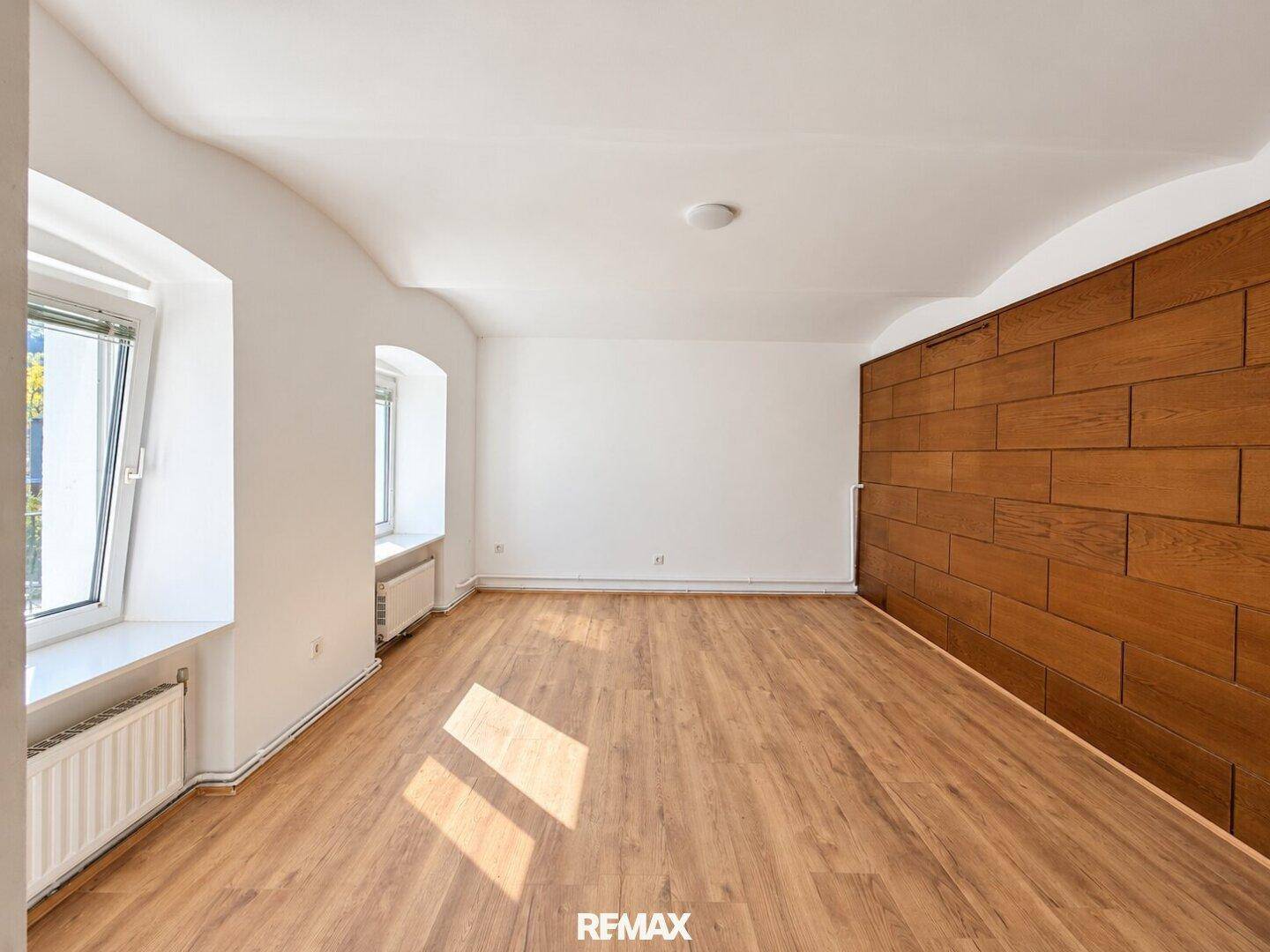 Heller Raum mit Holzplankenboden, weiß gestrichenen Wänden und einer Holzwand.