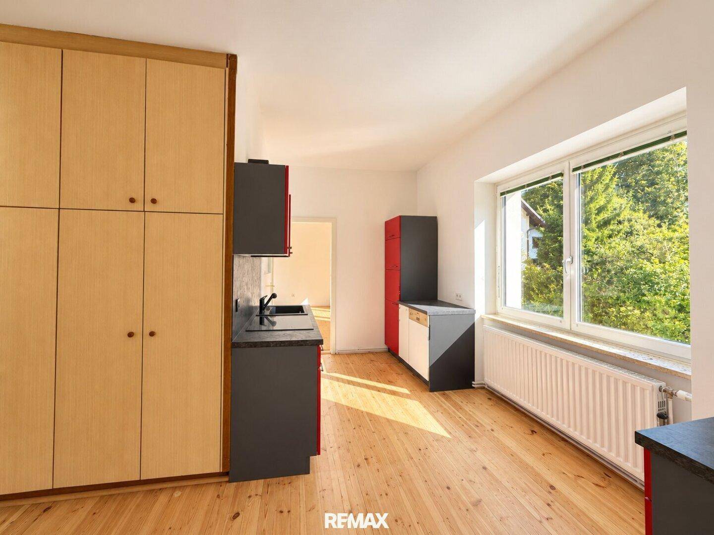 Küche mit Holzschränken, roten und grauen Elementen und Blick ins Grüne.