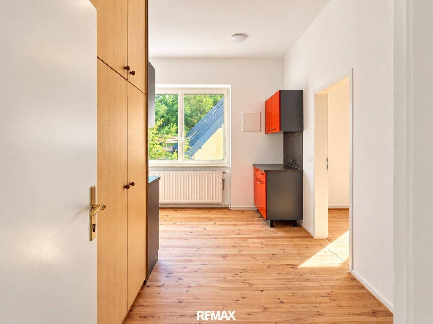Küche mit Holzboden, modernen Schränken und Zugang zu einem weiteren Raum.