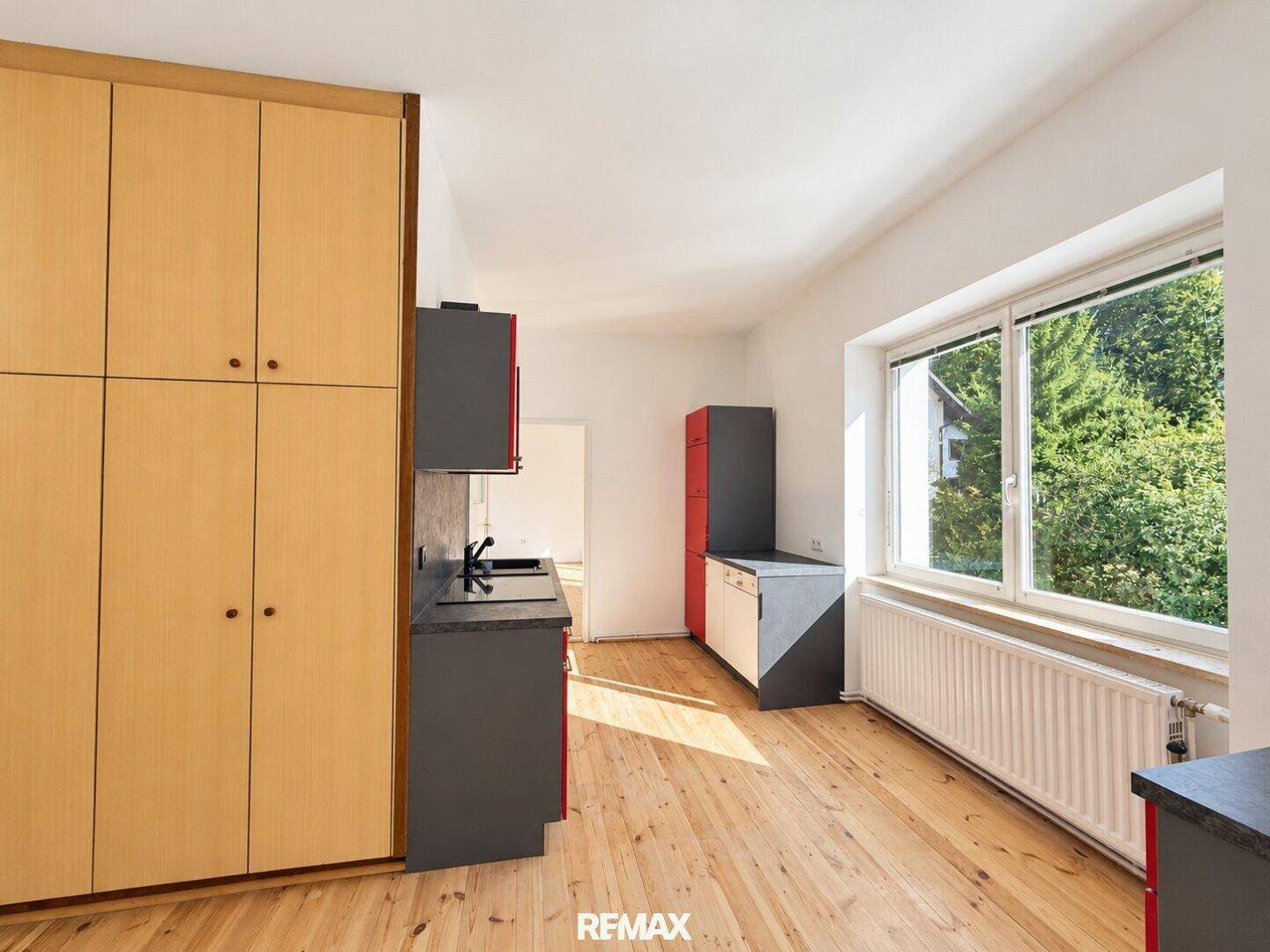Küche mit Holzschränken, roten und grauen Elementen und Blick ins Grüne.