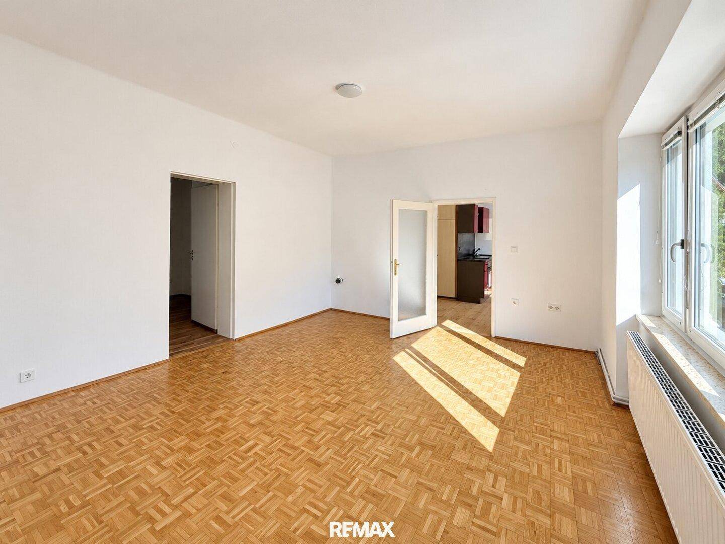 Geräumiges Wohnzimmer mit Parkettboden, weißen Wänden und Doppeltüren.