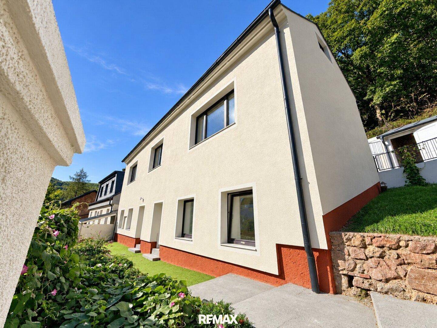 Moderne Gebäudefassade mit mehreren Fenstern und einer gepflegten Grünfläche im Vordergrund.