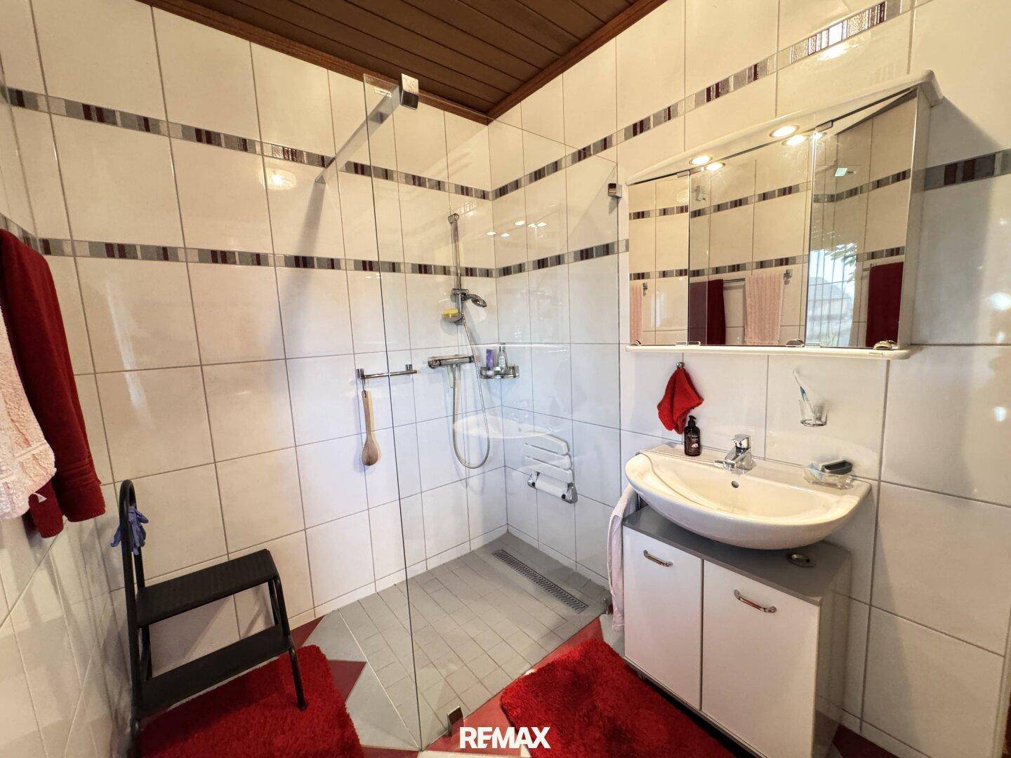 Badezimmer mit weiß-grauen Fliesen, Duschbereich und Waschtisch mit Spiegelschrank.