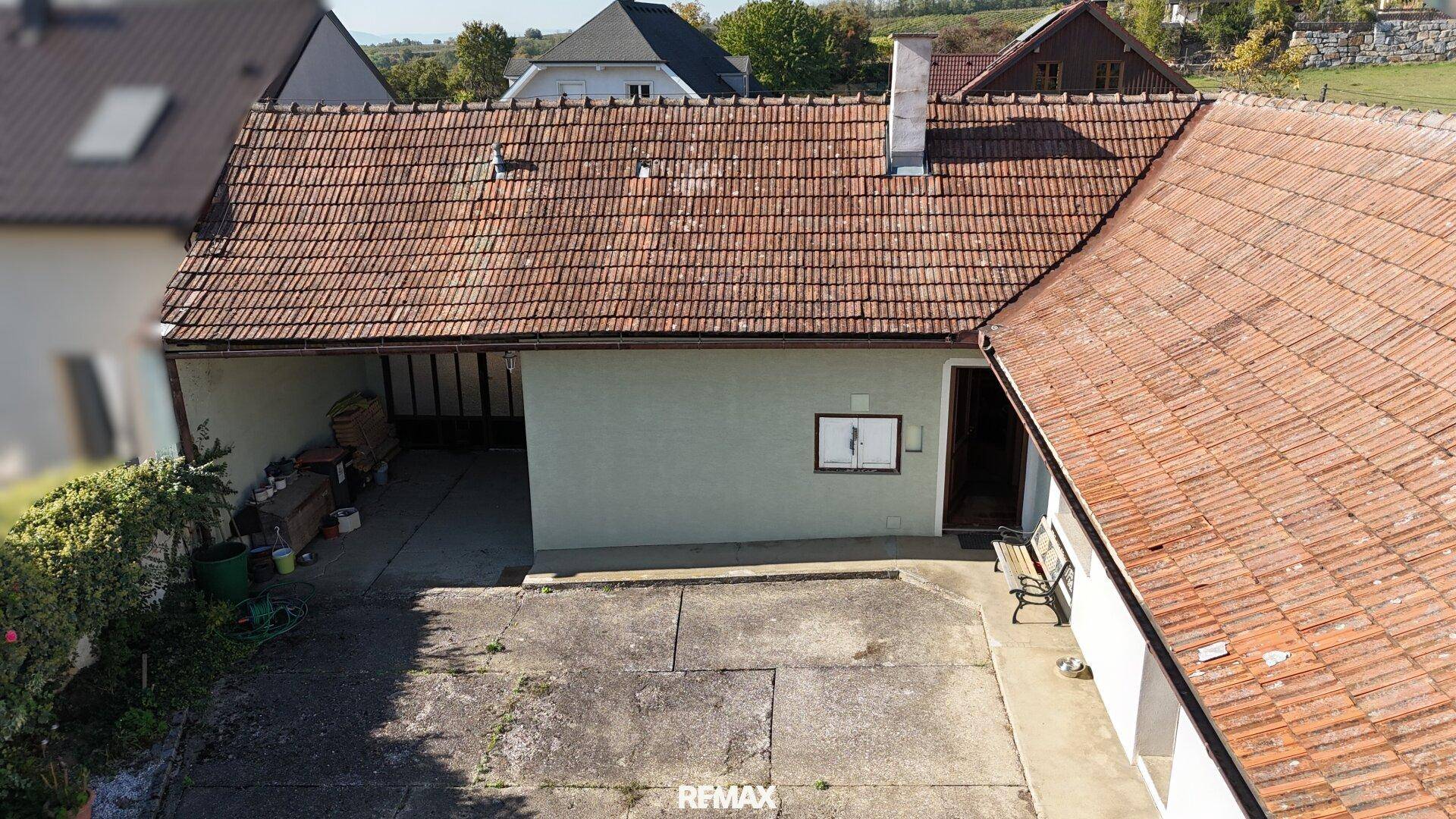 Luftaufnahme des hinteren Hofbereichs mit gepflasterter Fläche und überdachtem Stellplatz.