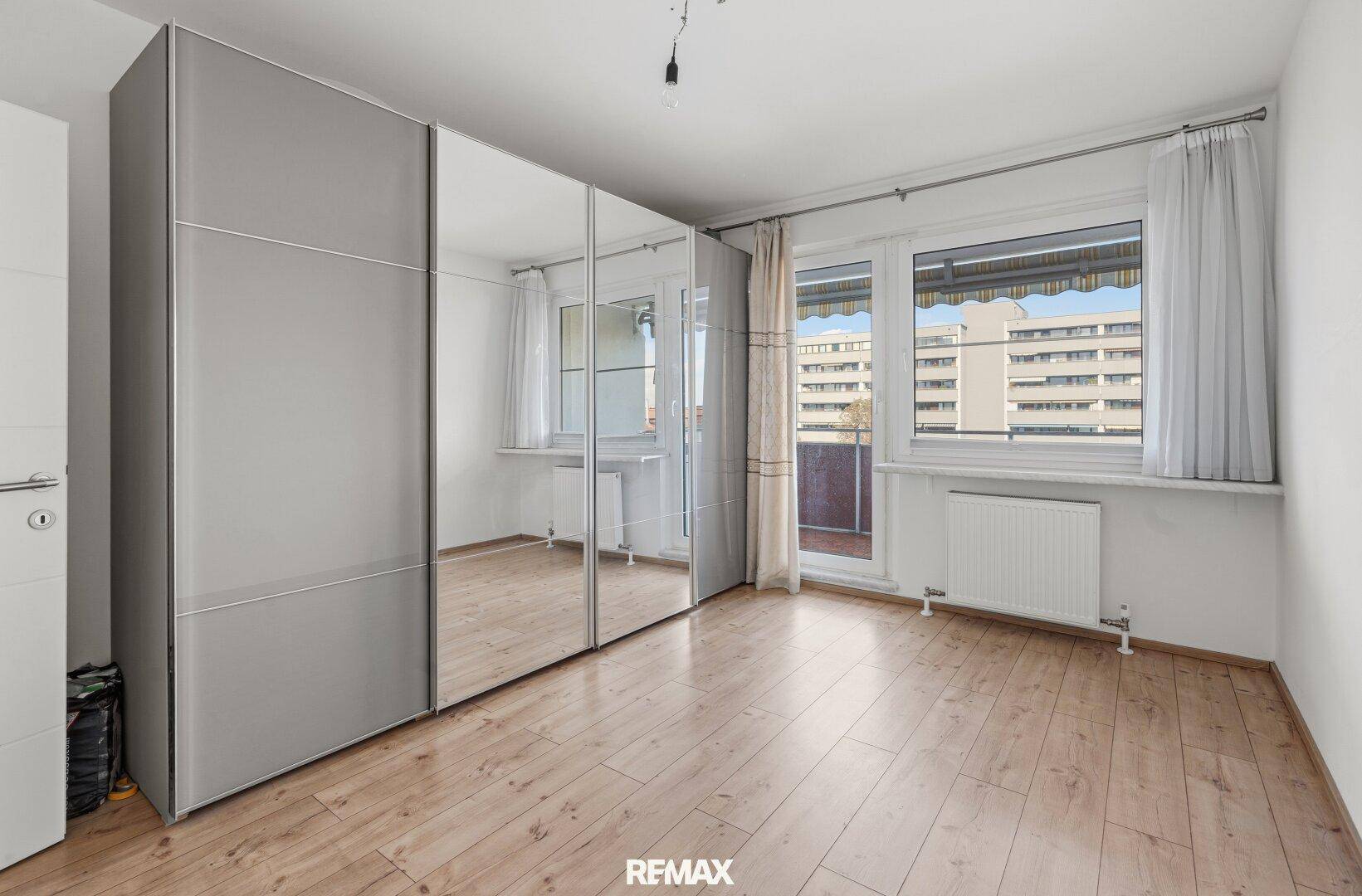 Schlafzimmer mit großem Spiegelschrank, Holzfußboden und Blick auf umliegende Gebäude.