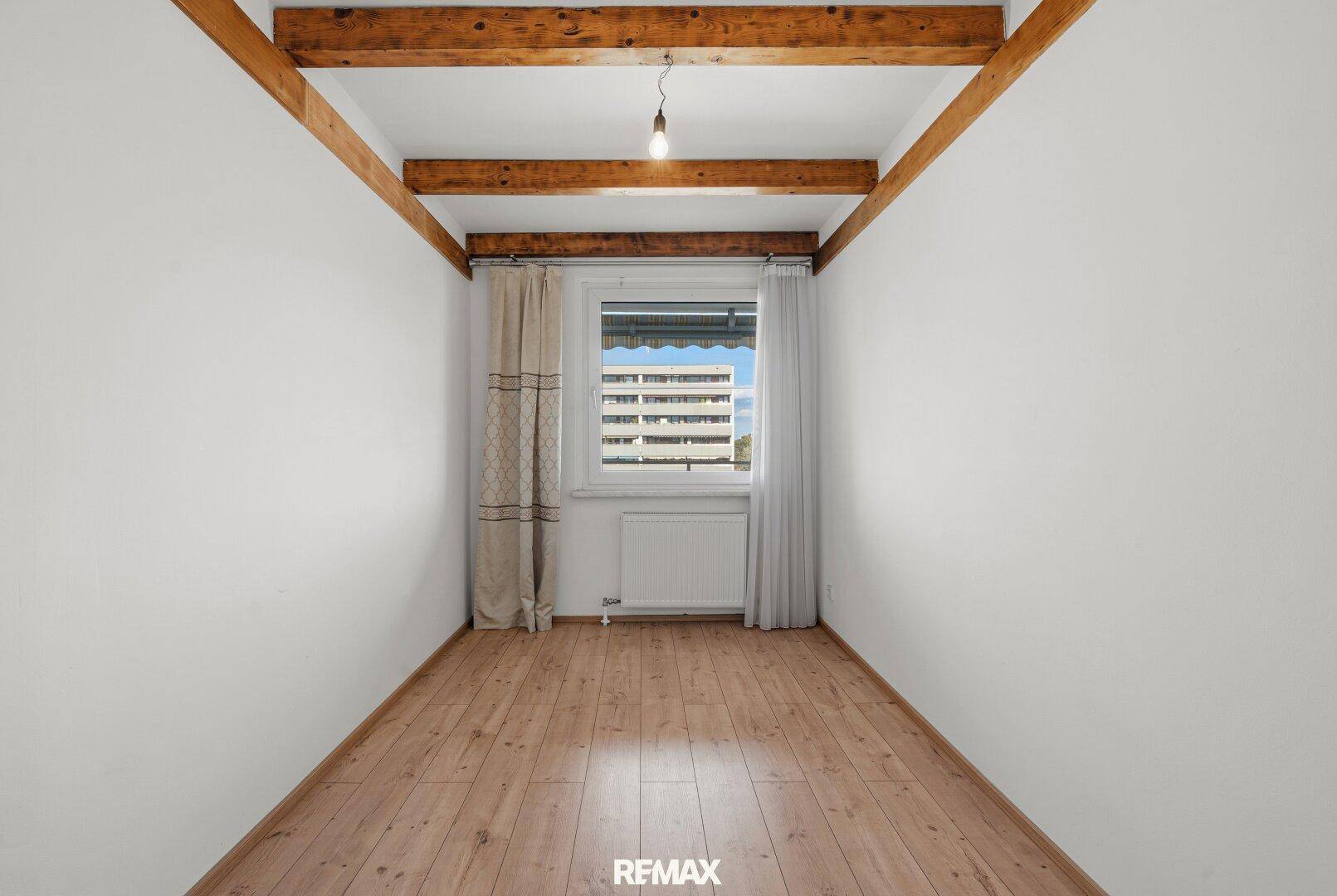 Kleiner Raum mit sichtbaren Holzbalken an der Decke, Holzfußboden und Fenster.
