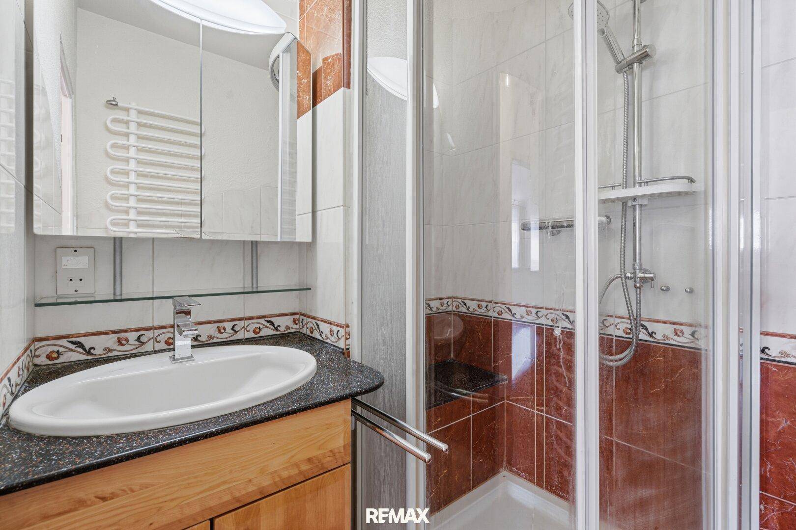 Badezimmer mit Duschkabine, Waschtisch, Spiegelschrank und beheiztem Handtuchhalter.