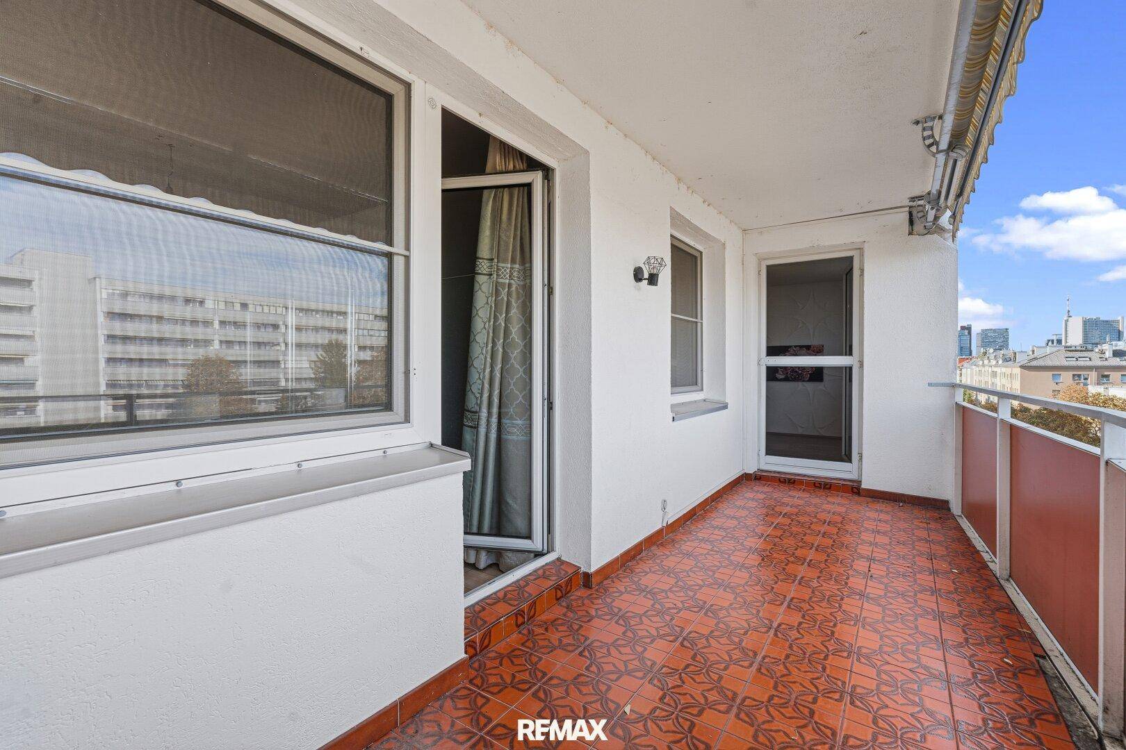 Geräumiger Balkon mit gemusterten Fliesen, Markise und Blick auf die Umgebung.