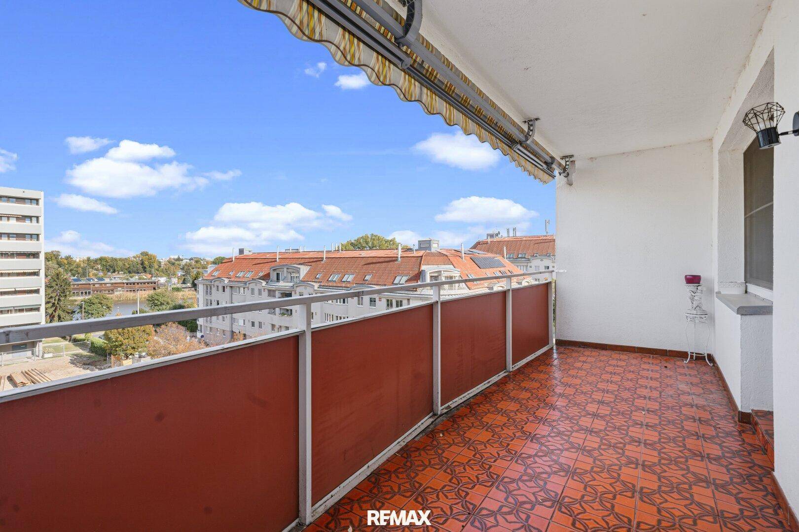 Großer Balkon mit Markise, gemusterten Fliesen und weitem Blick über die Stadt und Wasser.