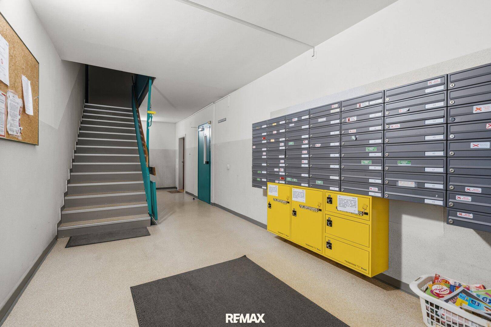 Eingangsbereich des Gebäudes mit Briefkästen, Treppenhaus und Informationswand.