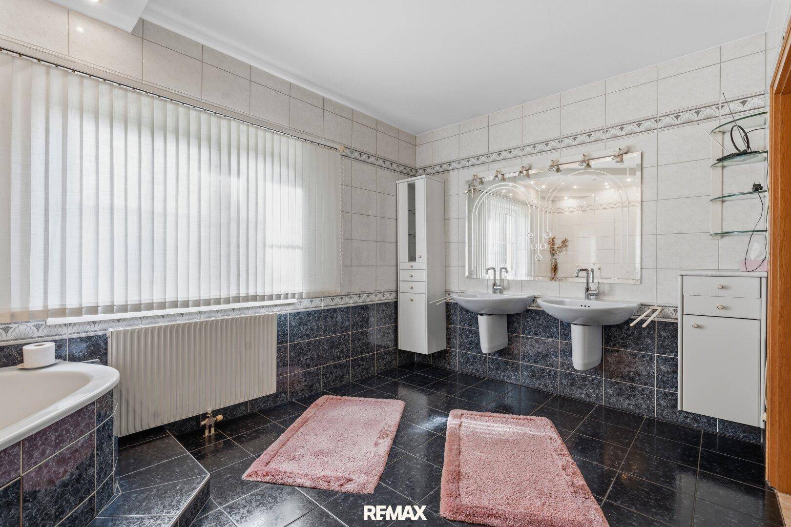 Geräumiges Badezimmer mit Doppelwaschbecken, Badewanne und dunklen Fliesen.